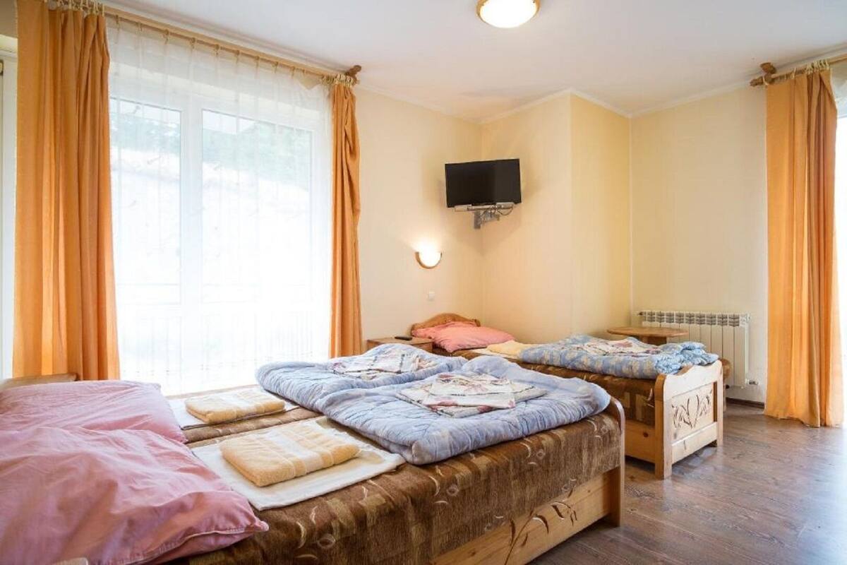 A room with two beds, a TV mounted on the wall, and a window with curtains.