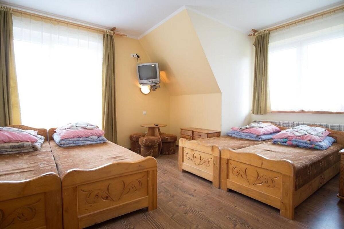 A room with four wooden beds, a small table, and a television mounted on the wall.