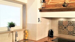 Una cocina con armarios de madera, un lavamanos de acero inoxidable, una ventana con planta y un salpicadero decorativo.