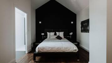 Un dormitorio moderno con cabecera negra, ropa de cama blanca y suelo de madera.