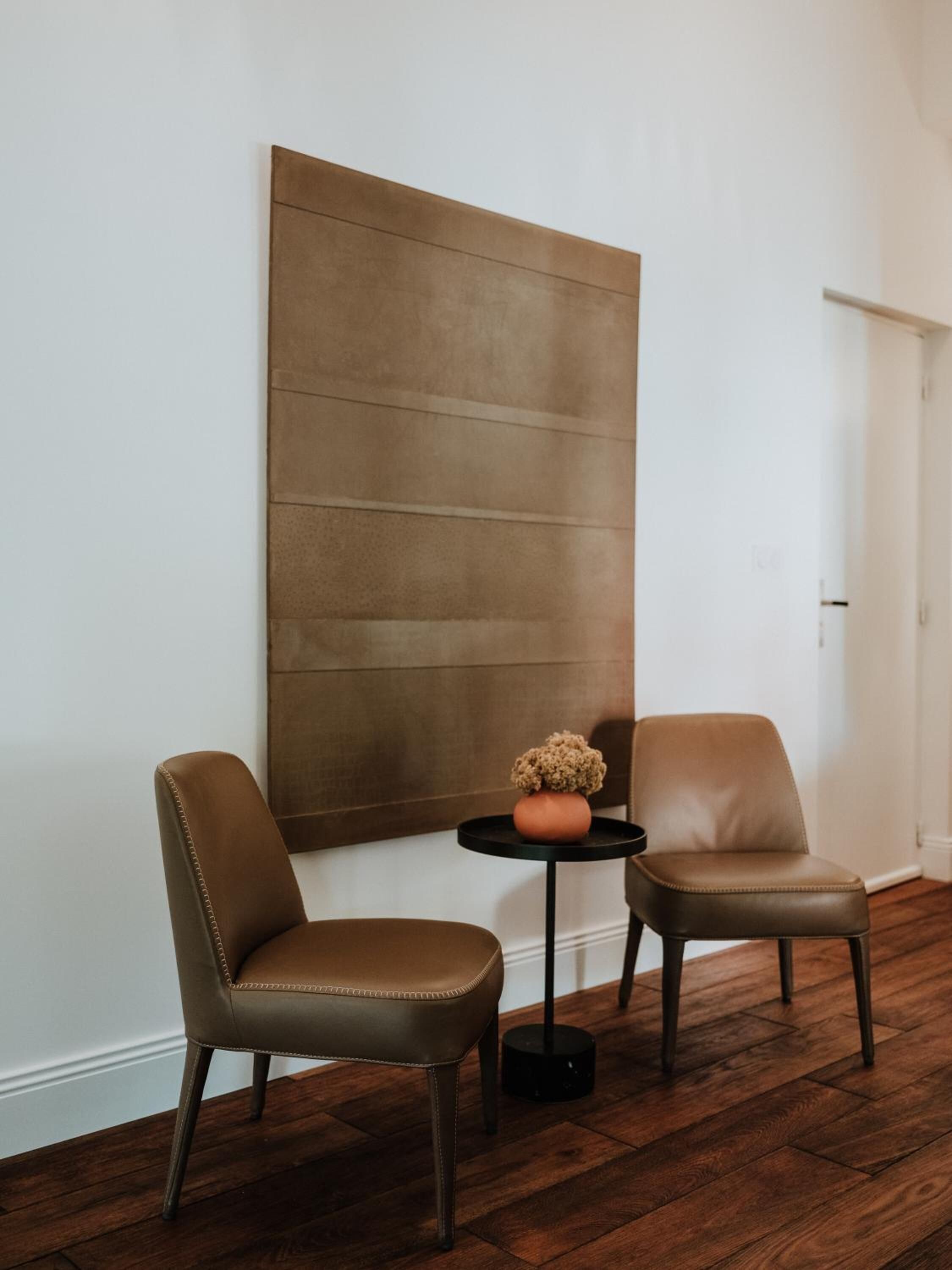 A room with two leather chairs, a round black table, and a large abstract painting on the wall.