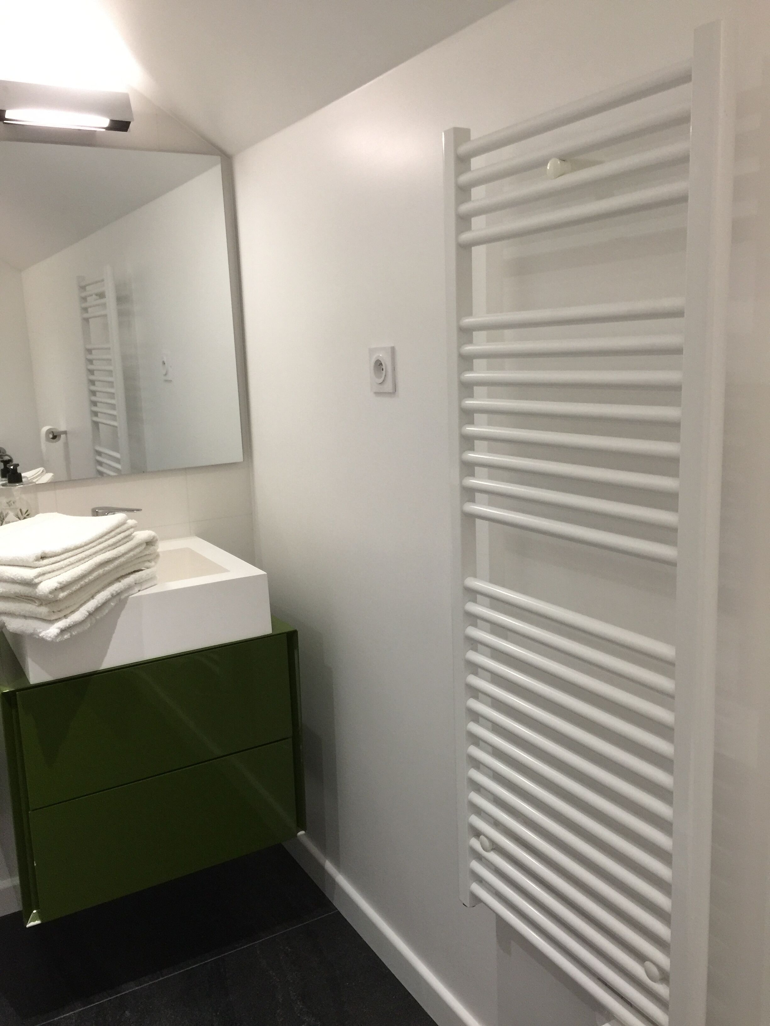 Ein Badezimmer mit einem weißen Waschbecken, einem grünen Schrank und einem Stapel weißer Handtücher.