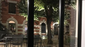 A view through a glass door of an outdoor patio area with a table and chairs, a tree, and a brick building in the background. - Le clos de la Pomponnette (Pomponne)
