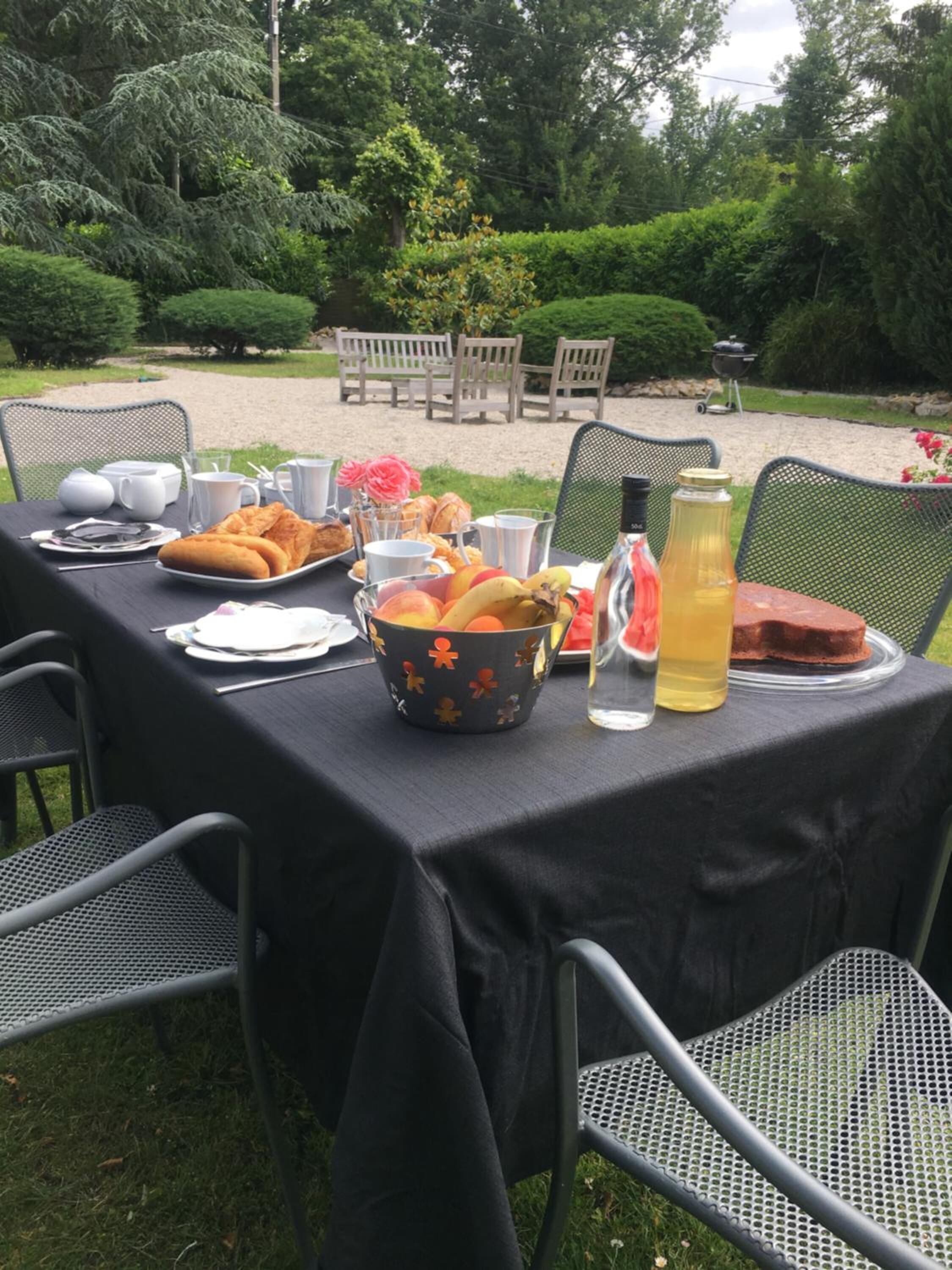 Une table à manger d’extérieur, dressée avec des assiettes, des couverts, un saladier de fruits et une carafe de limonade.