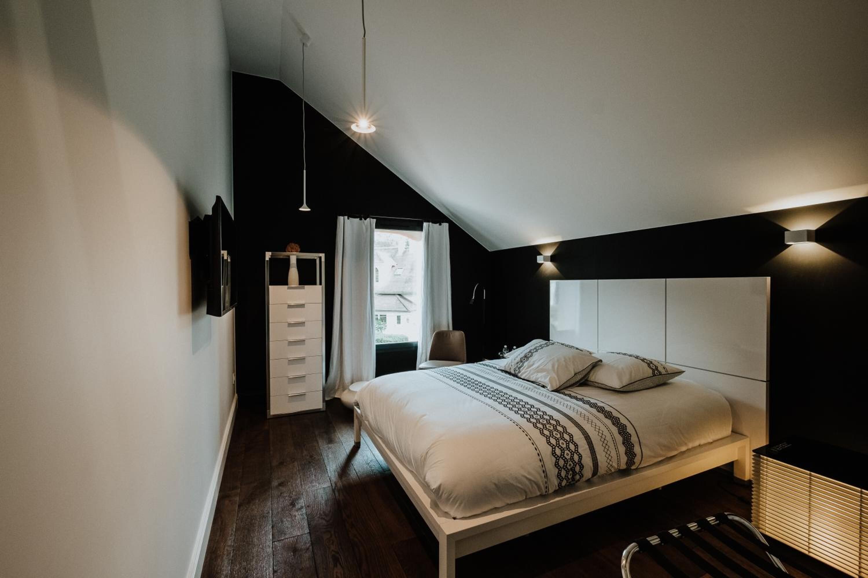Une chambre à coucher avec un lit, une commode, une chaise et une fenêtre avec des rideaux.