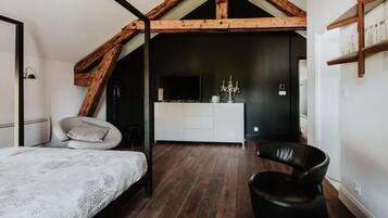A bedroom with a bed, a chair, a vanity with a mirror, and a television.