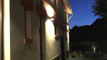 Een gevel bij zonsondergang met verlichte architectonische details en een verhard pad dat leidt naar een terras.