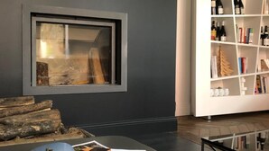 A modern room with a dark wall, a framed artwork, a bookshelf with books and bottles, a coffee table with a magazine and a cup, and a bed with a pillow. - Le clos de la Pomponnette (Pomponne)