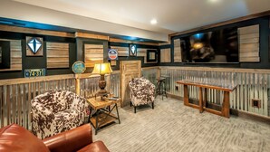 Un espace salon accueillant avec un canapé en cuir, un fauteuil à motifs, une table basse en bois et un téléviseur fixé au mur.