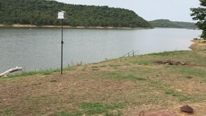 Zona junto al lago con un campo cubierto de césped, un banco de madera y una estructura blanca sobre un poste.