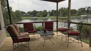 Una terraza techada al aire libre con suelo de madera, sillas rojas acolchadas y una mesa de metal.