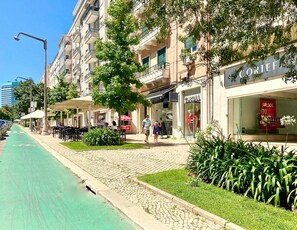 Une rue avec une piste cyclable, des terrasses et des devantures de magasins, dont une affiche bien visible indiquant « CORTEF ».