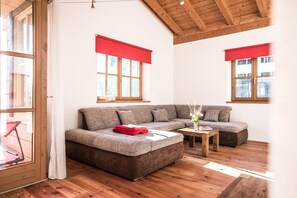 Un salon moderne avec un canapé d’angle, un plancher en bois et de grandes fenêtres agrémentées de rideaux rouges.