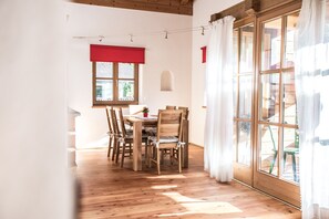 A dining area with a wooden table and chairs, a window with red curtains, and a view of the outdoors.