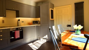 A modern kitchen with grey cabinets, a microwave, and a toaster. There is a dining table with chairs and a vase of flowers. - 14 St Saviour's Place (York)