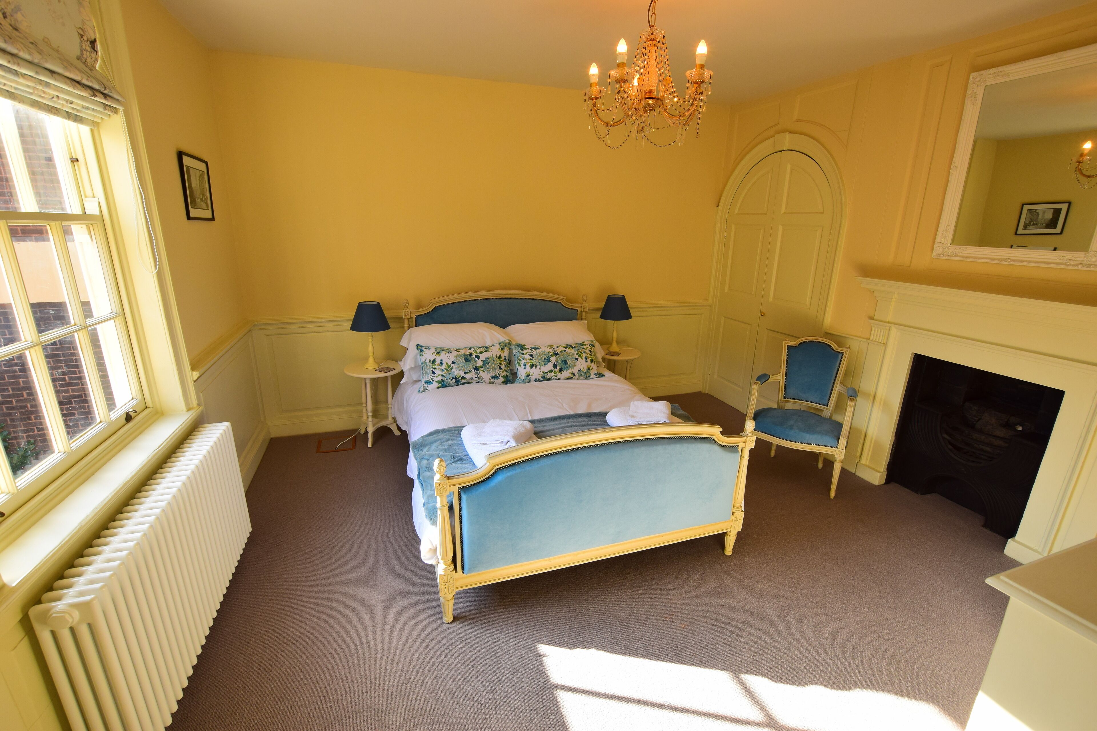 A bedroom with a bed, two bedside tables, a chair, a fireplace, and a window.