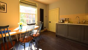 A kitchen with a dining table, chairs, a window with blinds, a door, and a countertop with various items. - 14 St Saviour's Place (York)