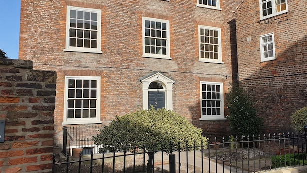 A multi-story brick building with white-framed windows, a central door with a small porch, and a black metal fence in front. - 14 St Saviour's Place (York)