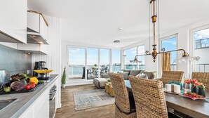 A modern kitchen with a view of the sea, a dining area with wicker chairs, and a large window overlooking the ocean. - Water house "Villa Sansibar" - special Baltic Sea vacation with roof terrace and sauna (Olpenitz)