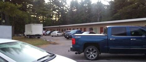 A parking lot with several vehicles, including a white car and a blue pickup truck, in front of a building with multiple rooms.