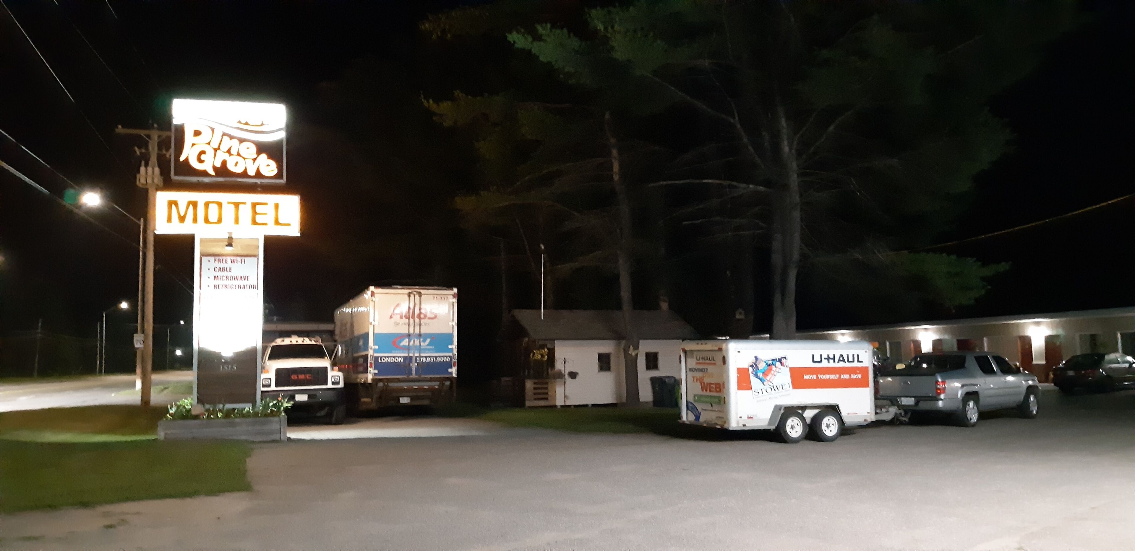 A motel with a neon sign, a delivery truck, and a U-Haul trailer parked in front.