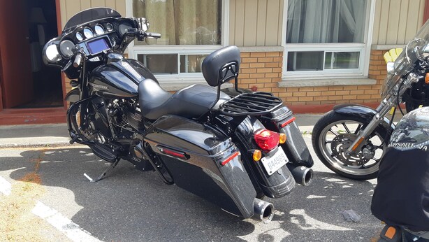 A black motorcycle parked in front of a building with a brick facade and a window with white frames. - Pine Grove Motel (Sault Ste. Marie)