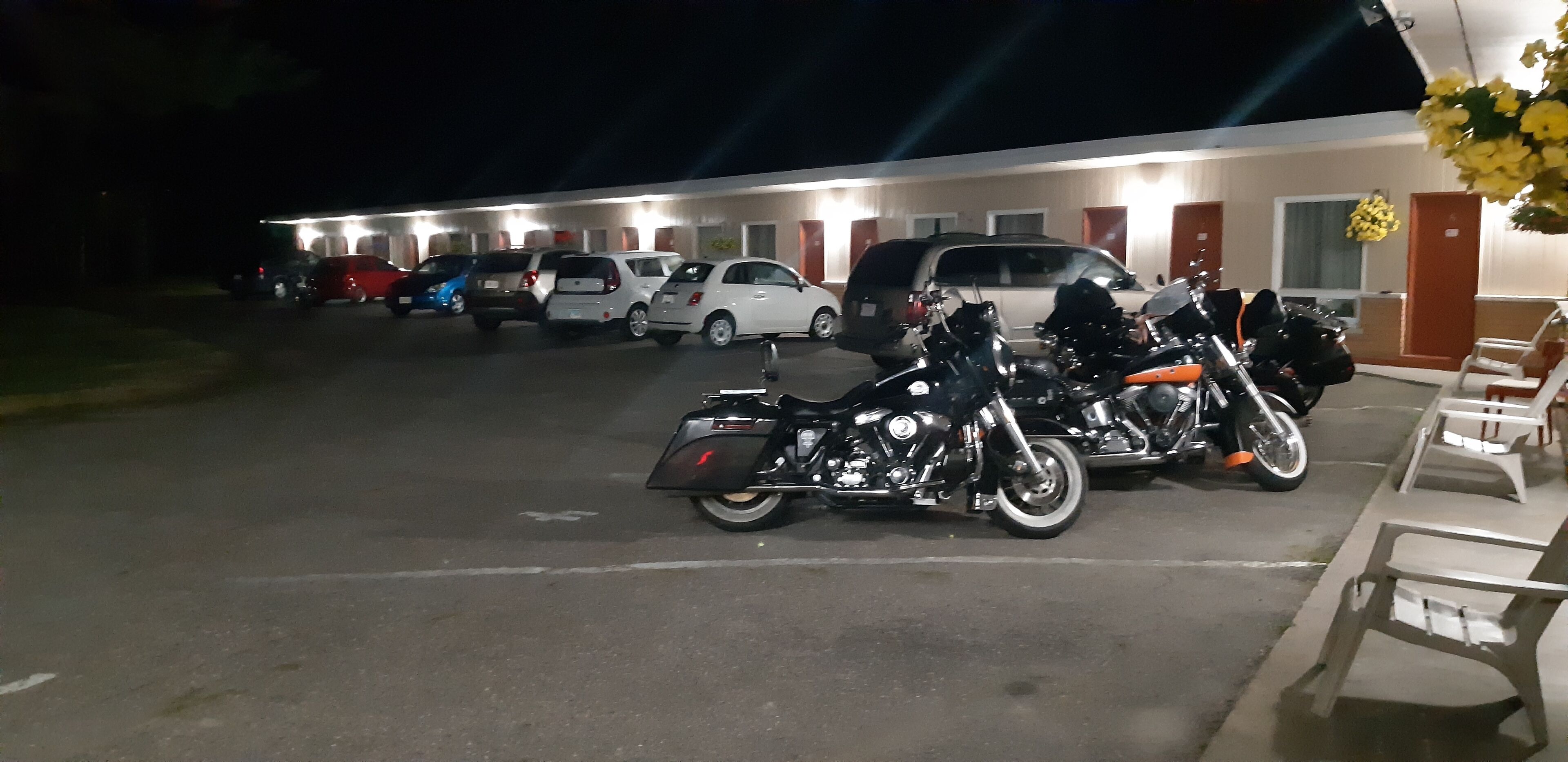 A parking lot with several motorcycles and cars parked in front of a motel with multiple rooms.