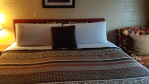 A neatly made bed with a striped blanket, a bedside lamp, and a floral-patterned chair. - Pine Grove Motel (Sault Ste. Marie)