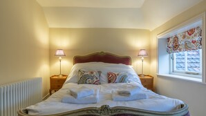 A neatly made bed with a red headboard, two bedside tables with lamps, and a window with a decorative valance. - 71 Micklegate - Apartment 1 (York)