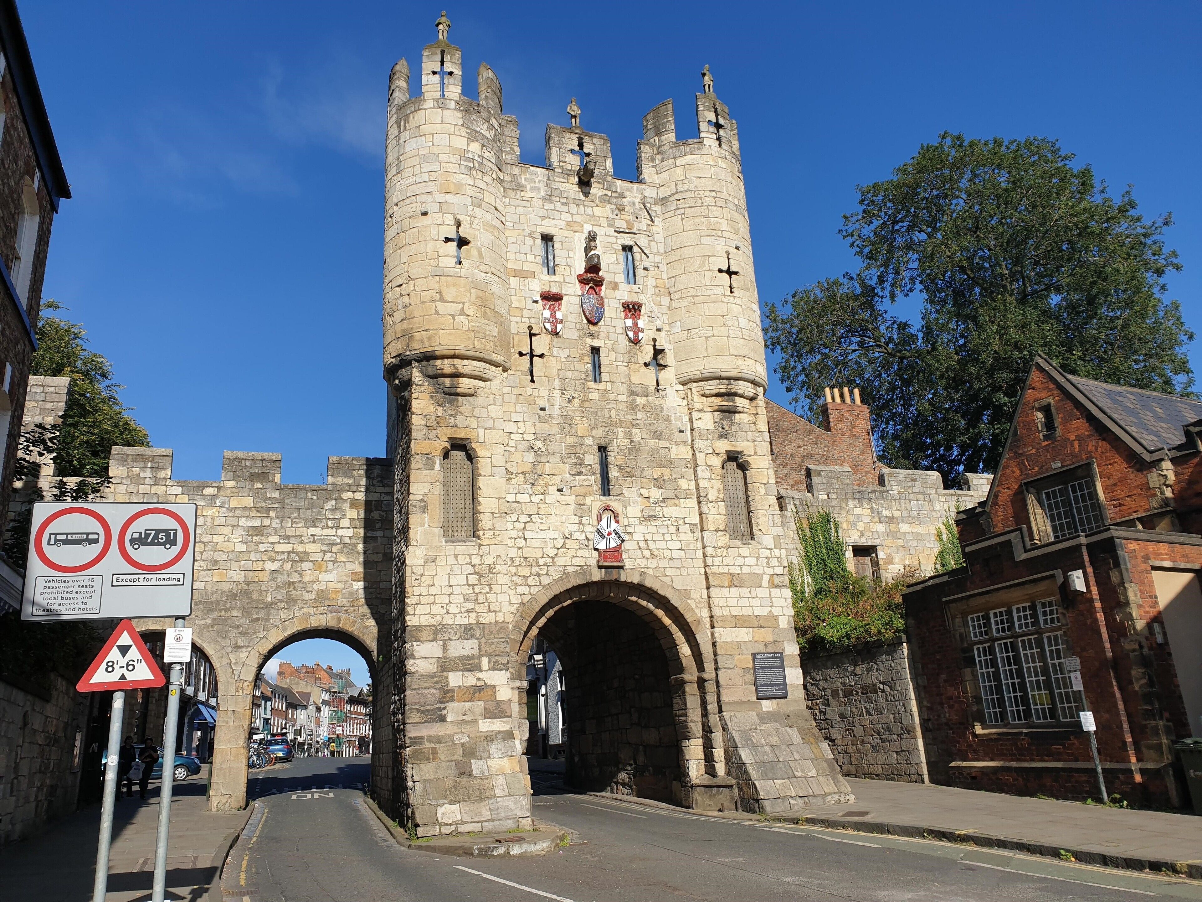 A historic stone tower with a narrow entrance, signs indicating height restrictions, and a plaque.