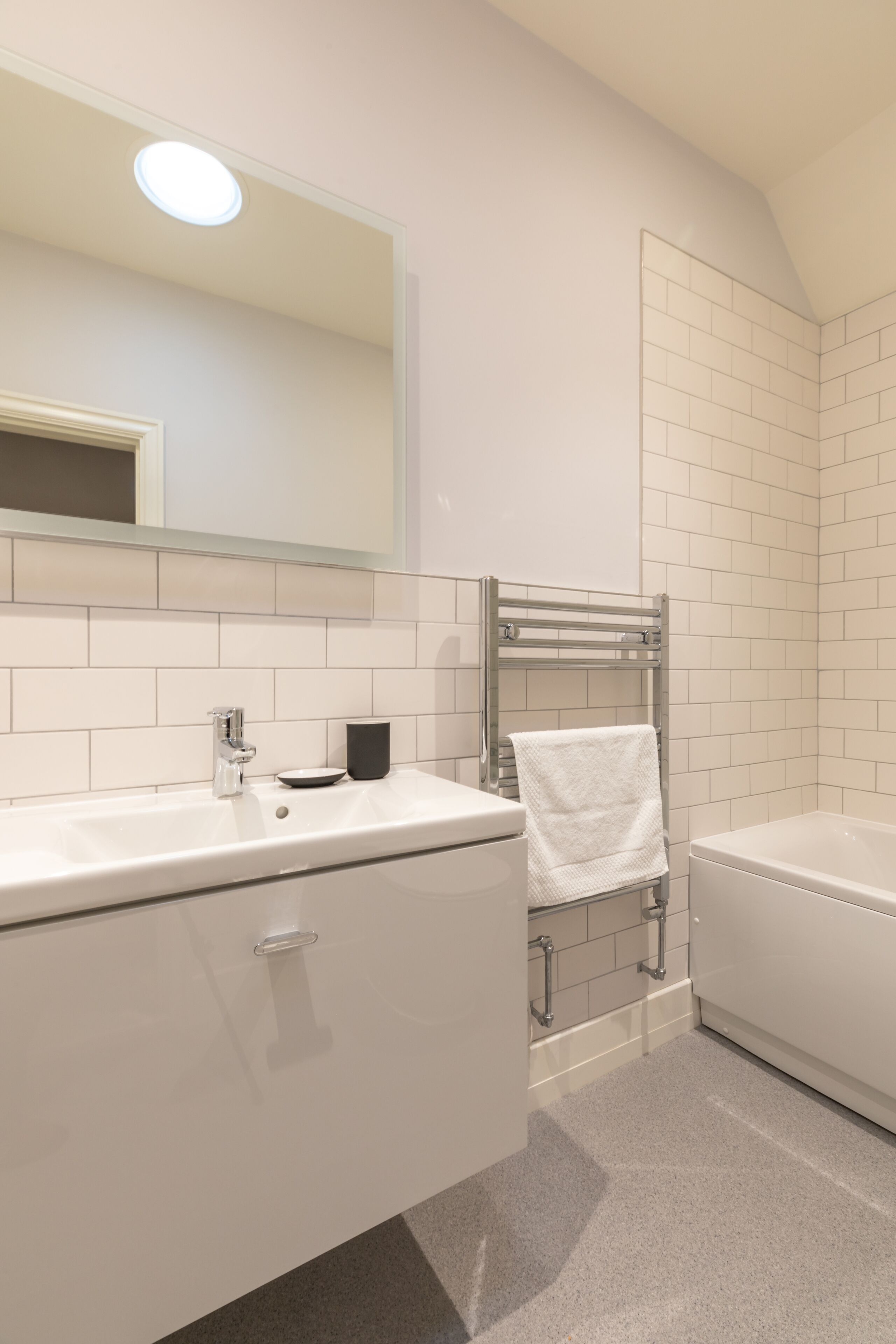 A modern bathroom with a white vanity, a bathtub, and a towel rack.
