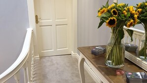 A hallway with a white door, a wooden bench, a vase with sunflowers, and a mirror on the wall. - 71 Micklegate - Apartment 1 (York)