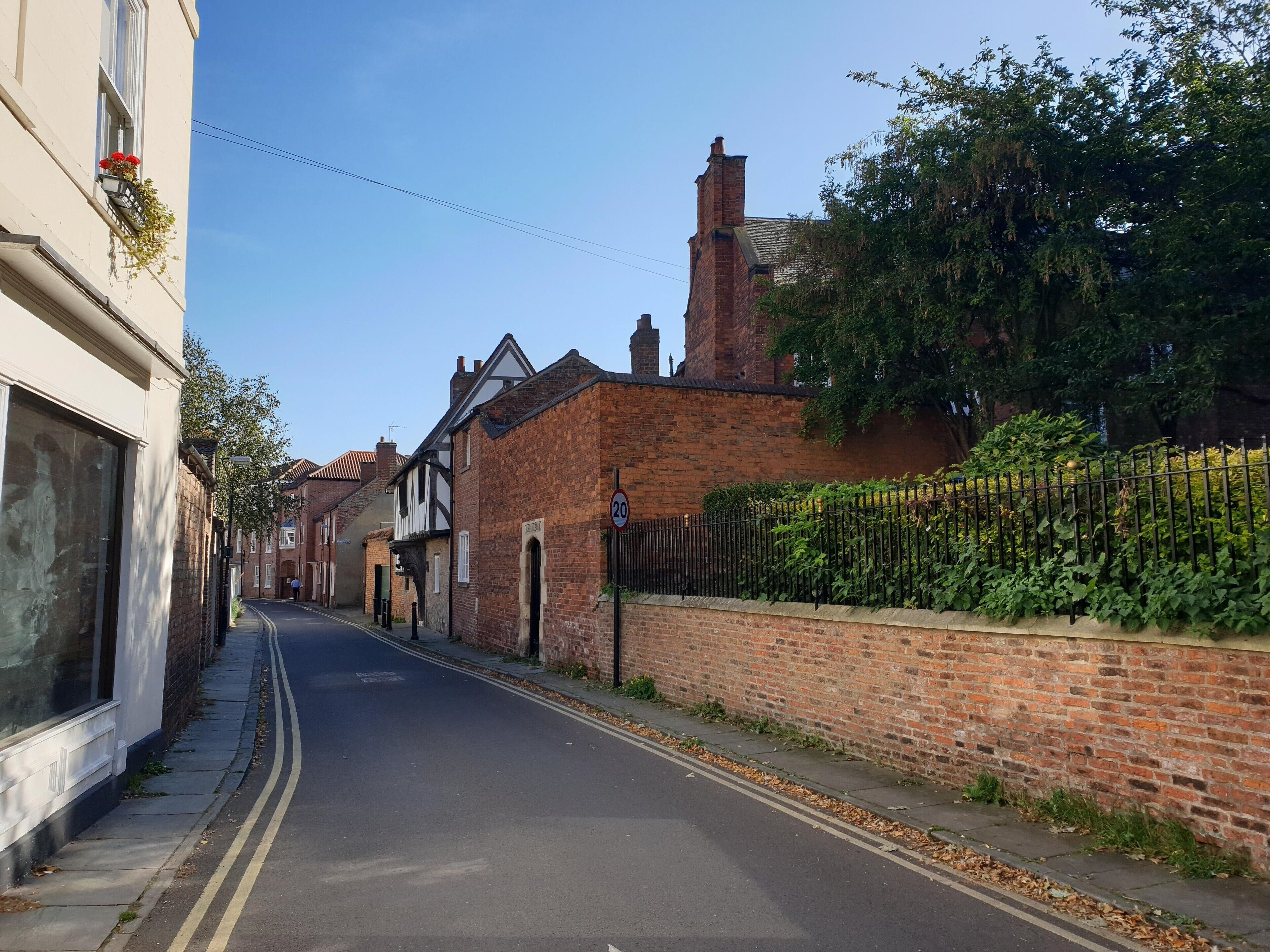 A narrow street lined with traditional brick houses, a clear blue sky, and a speed limit sign of 20.