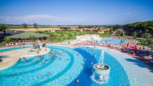 A large outdoor swimming pool with multiple lanes, a central fountain, and surrounding lounge areas with umbrellas. - Happy Camp in Camping Village California (Montalto di Castro)