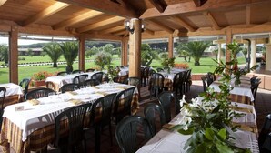 An outdoor dining area with tables set for two, covered by a wooden roof, and surrounded by chairs. - Happy Camp in Camping Village California (Montalto di Castro)