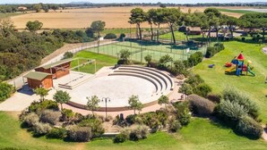 An outdoor amphitheater with tiered seating, surrounded by greenery and a playground. - Happy Camp in Camping Village California (Montalto di Castro)