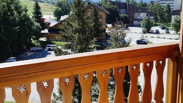 A mountain view with a wooden balcony railing, a restaurant, and a parking lot.