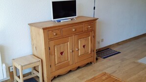 A wooden cabinet with a television on top, a small wooden stool, and a patterned rug on the floor.