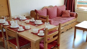 A dining area with a wooden table set for four, surrounded by red cushioned chairs.