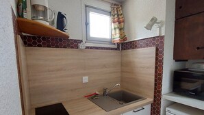 Une cuisine de taille réduite, dotée d’un plan de travail en bois, d’un évier et d’une fenêtre agrémentée d’un rideau.
