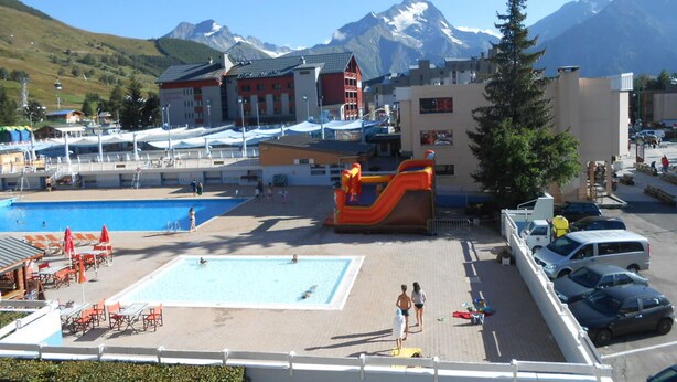 Un espace piscine doté d’un toboggan, entouré de bâtiments et avec des montagnes en arrière-plan.