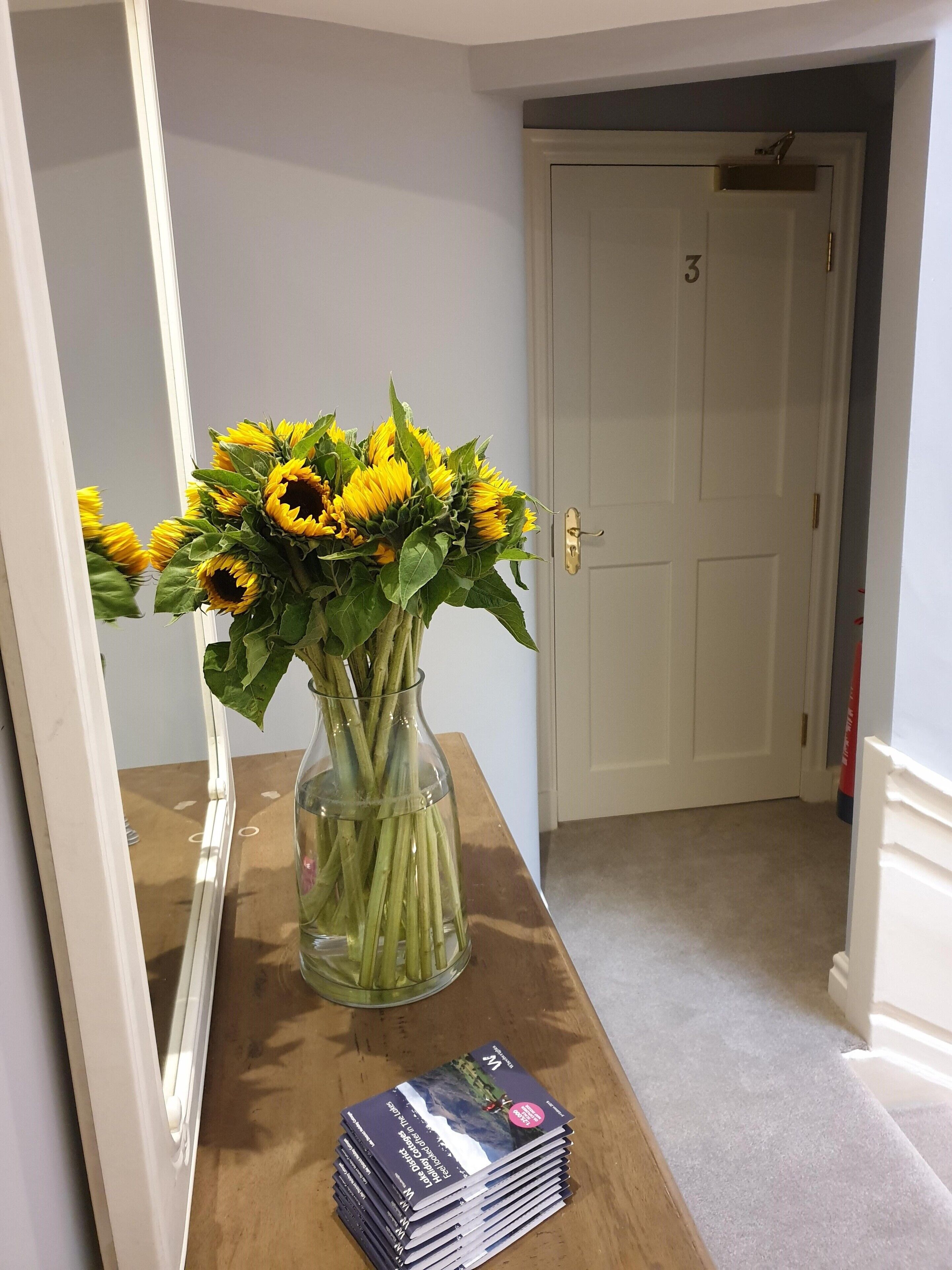 Une table en bois sur laquelle se trouve un vase rempli de tournesols et une pile de magazines.