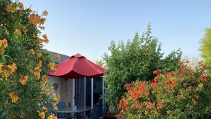 En udendørs patio med rød parasol, et bord med stole og en kaktusskulptur.