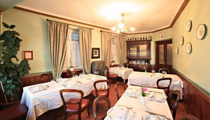 Une salle à manger avec deux tables dressées pour quatre personnes, des chaises en bois, un lustre et un buffet aux portes vitrées.