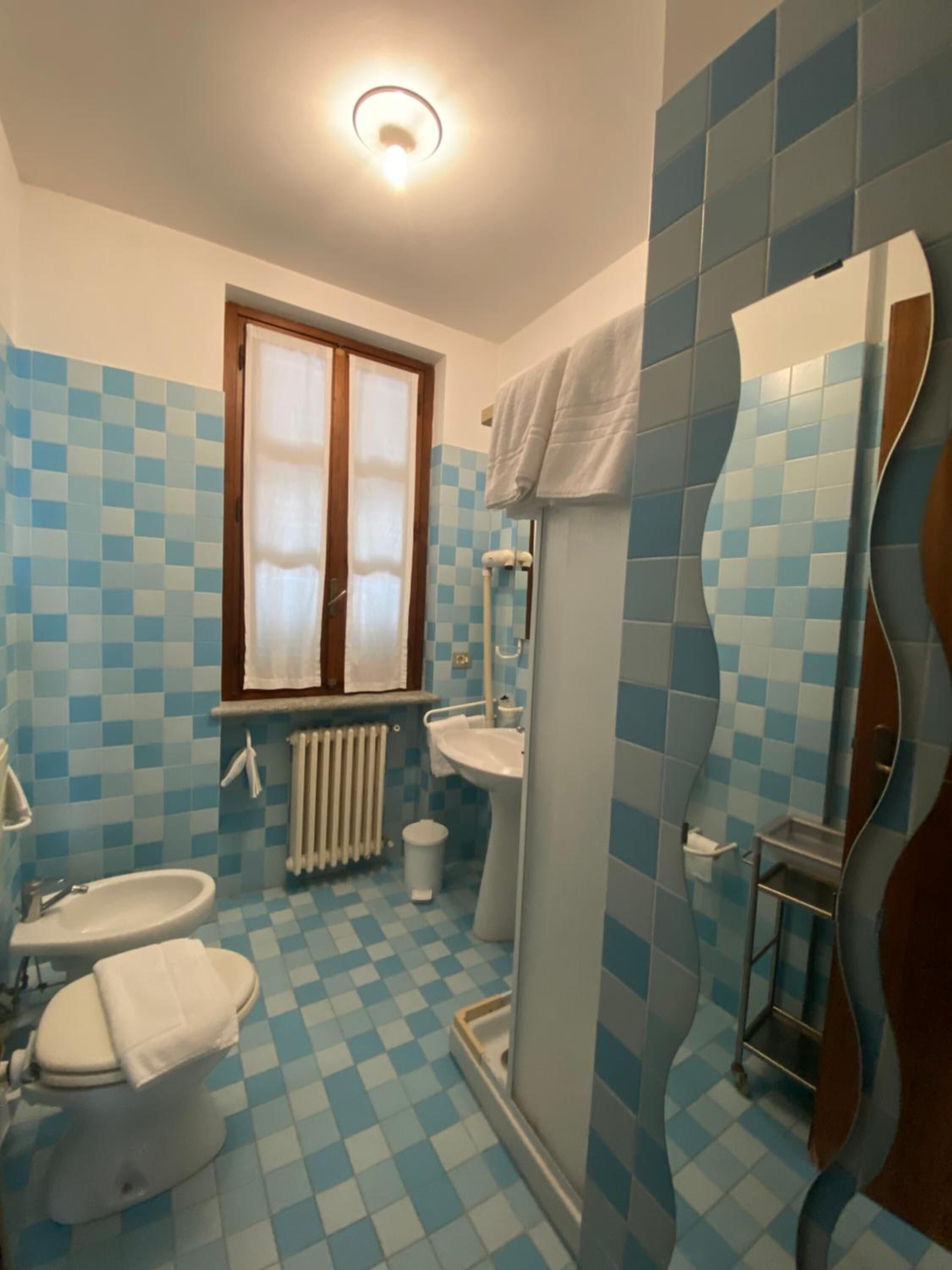Een badkamer met een zwart-wit schakeerd vloer, een raam met gordijnen, een wastafel, een toilet en een douche.