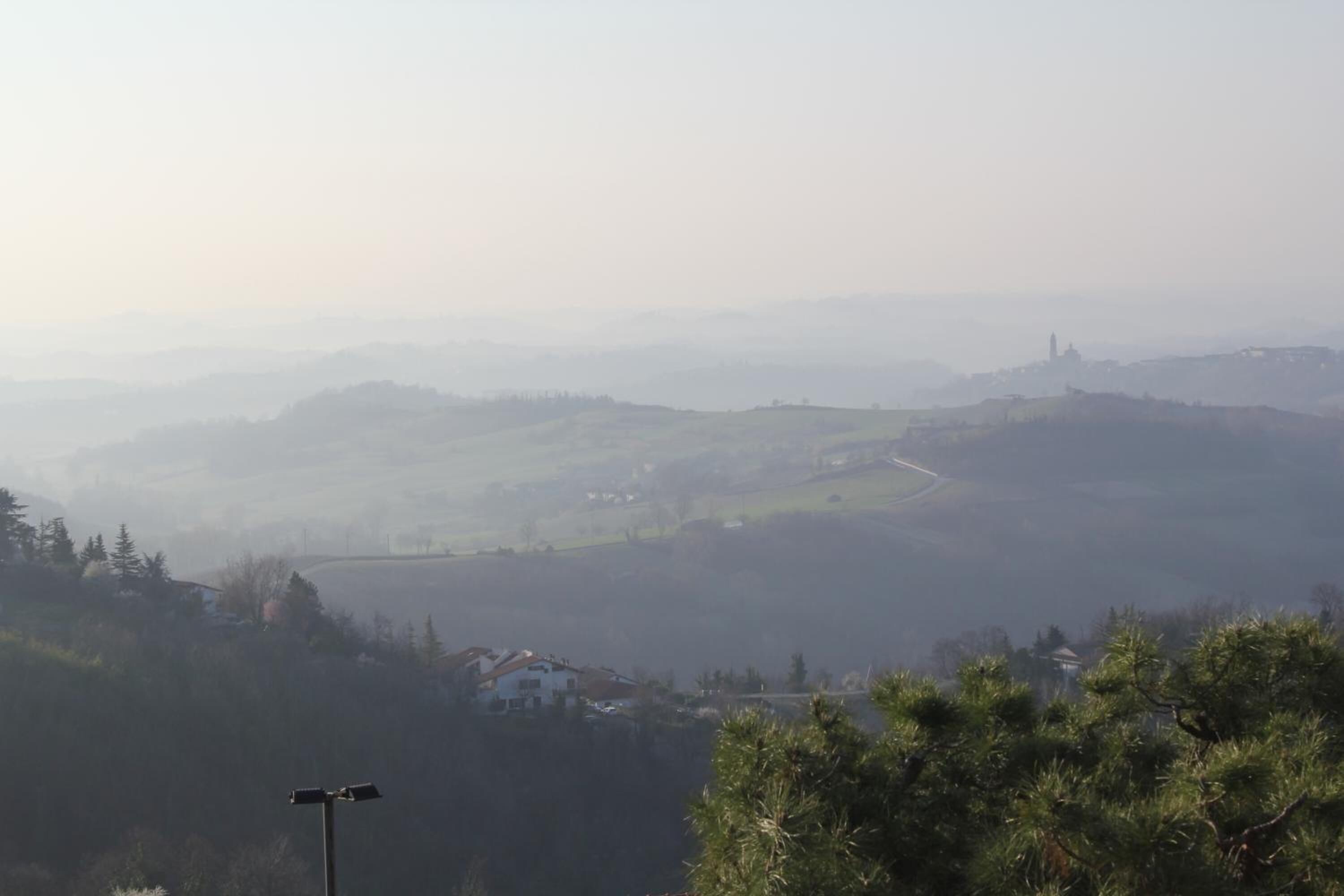 Vista panorámica de un paisaje montañoso con una torre distante, una carretera y algunos edificios.