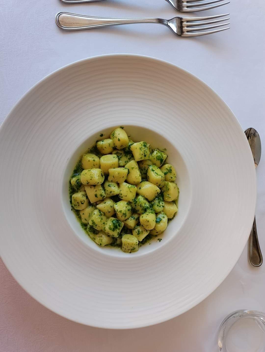 A white bowl of gnocchi with a green herb sauce on a white table.