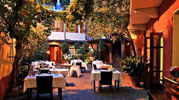 An outdoor dining area with tables and chairs, surrounded by lush greenery and a building with a tiled roof. - Albergo Cannon D'Oro (Cocconato)