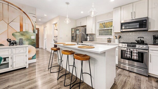 A modern kitchen with white cabinetry, a stainless steel oven, and a central island with stools. - Hot Tub | New Build | Sauna | Game Room | Walk Downtown | Theater | Arcade (Ann Arbor)