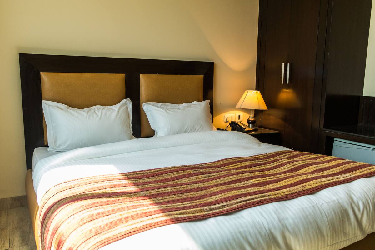 A neatly made bed with a striped blanket, a bedside lamp, and a wooden headboard.